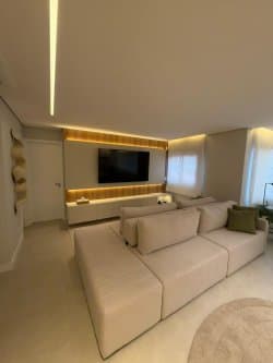 Sala de estar com sofá bege modular, iluminação em LED embutida e painel para TV.