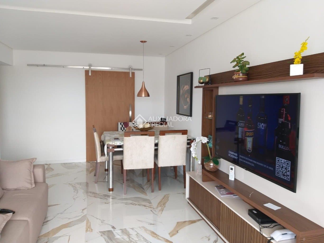 Sala de estar e jantar integrada com piso de mármore e TV instalada.
